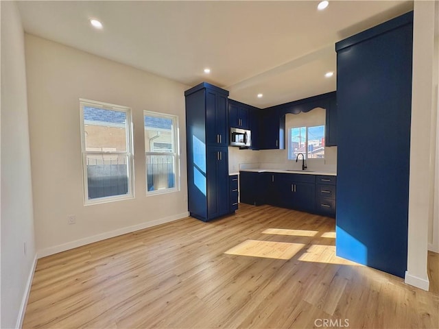 kitchen featuring light wood finished floors, stainless steel microwave, blue cabinetry, light countertops, and a sink