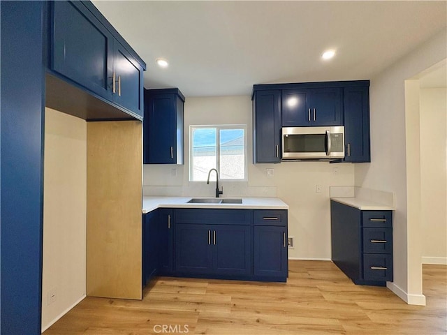 kitchen featuring stainless steel microwave, light wood-type flooring, blue cabinets, and a sink