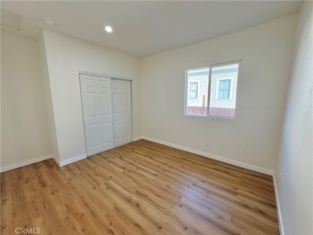 unfurnished bedroom with a closet, recessed lighting, light wood-style flooring, and baseboards