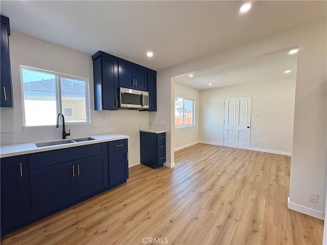 kitchen featuring a sink, stainless steel microwave, blue cabinetry, light wood-style floors, and light countertops