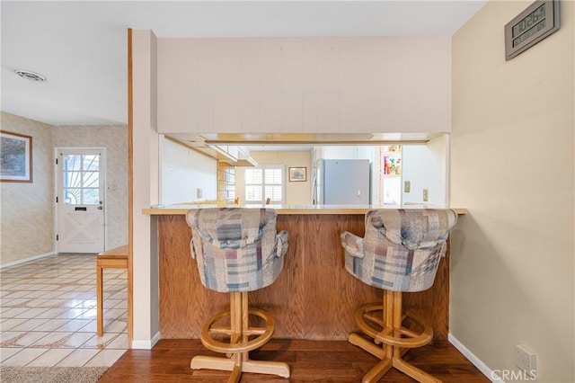 kitchen featuring baseboards, a kitchen breakfast bar, and freestanding refrigerator