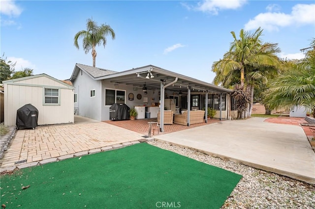 back of property featuring stucco siding, an outdoor structure, a patio area, a storage unit, and a ceiling fan