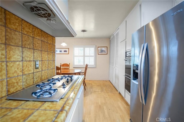 kitchen featuring visible vents, stainless steel refrigerator with ice dispenser, white cabinetry, stovetop, and light wood finished floors