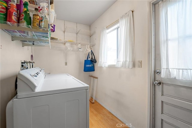 clothes washing area featuring baseboards, light wood-style flooring, laundry area, and washing machine and clothes dryer