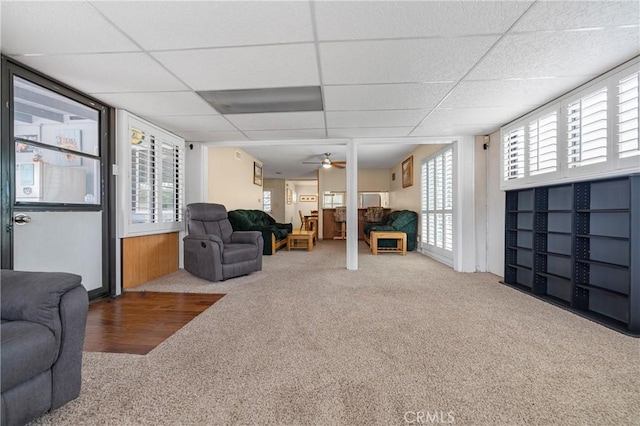 carpeted living room with a drop ceiling and a ceiling fan