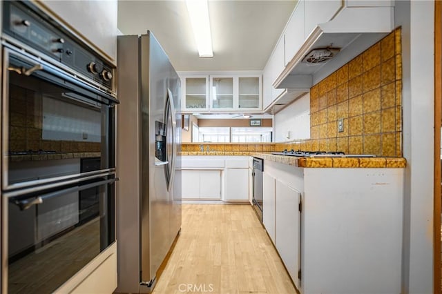 kitchen with tasteful backsplash, white cabinets, appliances with stainless steel finishes, and light wood-type flooring