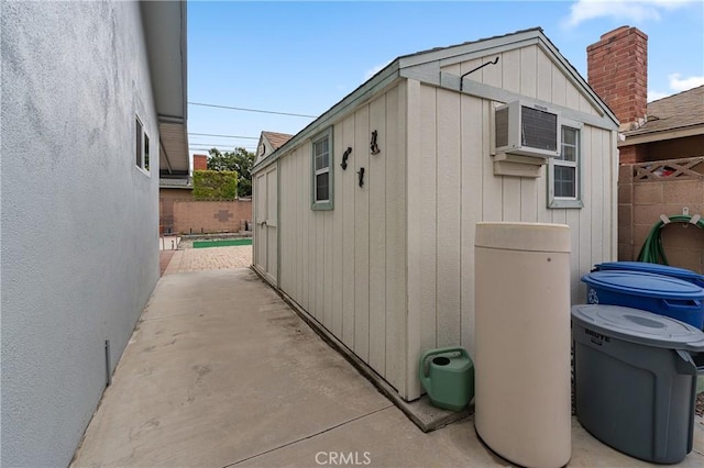 view of side of property with a patio area, a wall unit AC, an outdoor structure, and fence