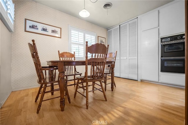 dining space with wallpapered walls, baseboards, visible vents, and light wood finished floors