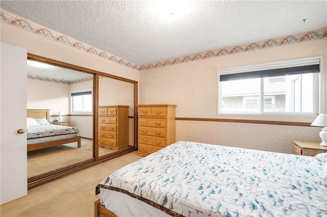 bedroom featuring a closet, light colored carpet, a textured ceiling, and wallpapered walls