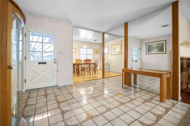 foyer with wallpapered walls, light tile patterned floors, visible vents, and baseboards