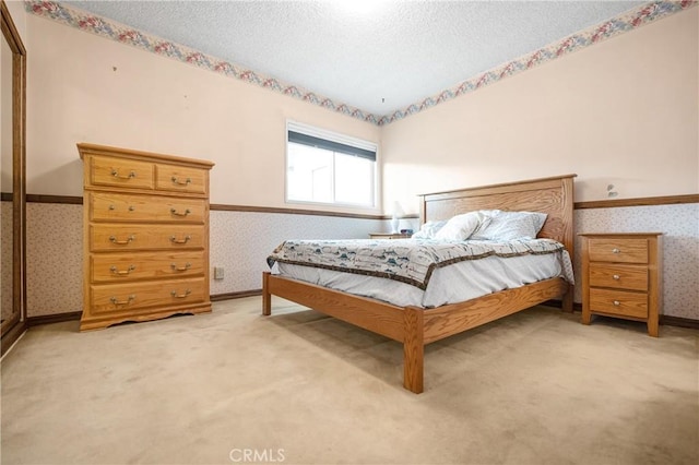 bedroom featuring light colored carpet, baseboards, a textured ceiling, and wallpapered walls