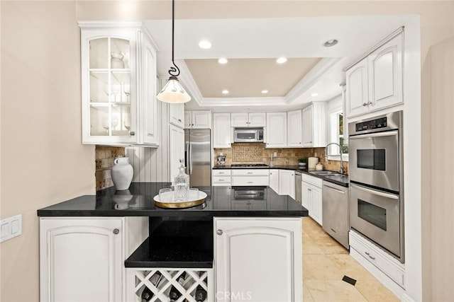 kitchen featuring a peninsula, a sink, stainless steel appliances, glass insert cabinets, and a raised ceiling