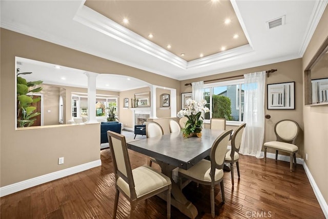 dining area with a tray ceiling, ornamental molding, decorative columns, a fireplace, and dark wood-style floors