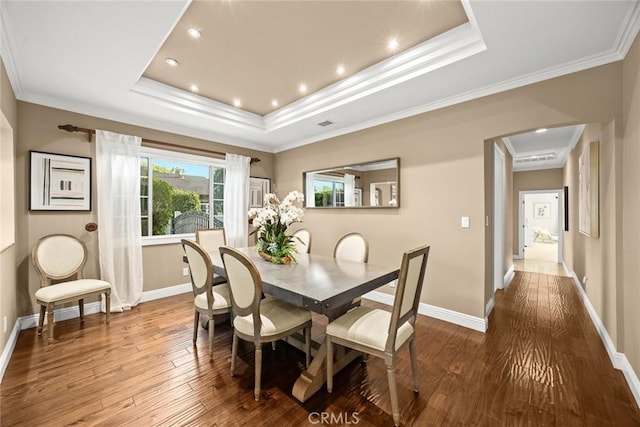 dining area featuring a raised ceiling, wood finished floors, and crown molding