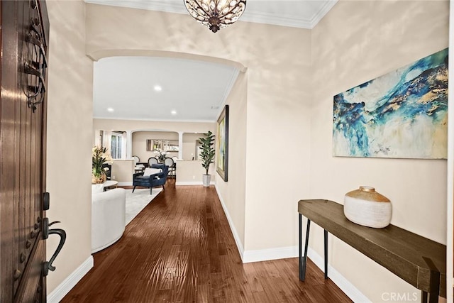 foyer entrance featuring baseboards, arched walkways, wood-type flooring, and ornamental molding