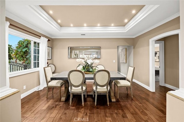 dining room with a tray ceiling, baseboards, wood finished floors, and ornamental molding