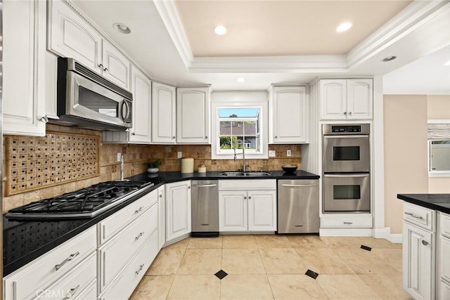 kitchen featuring dark countertops, a tray ceiling, appliances with stainless steel finishes, white cabinets, and a sink