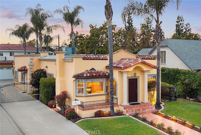 mediterranean / spanish home with stucco siding, a yard, a tile roof, and a gate