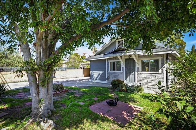 view of front of property with stone siding, a patio, and fence