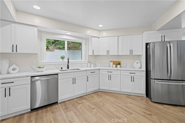 kitchen featuring light wood finished floors, recessed lighting, a sink, stainless steel appliances, and white cabinetry