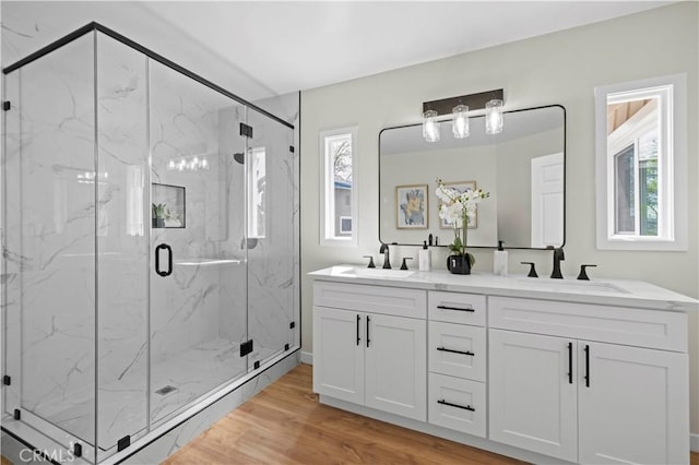 bathroom featuring double vanity, wood finished floors, a marble finish shower, and a sink