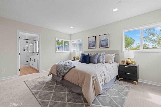 bedroom with recessed lighting, light colored carpet, baseboards, and ensuite bathroom