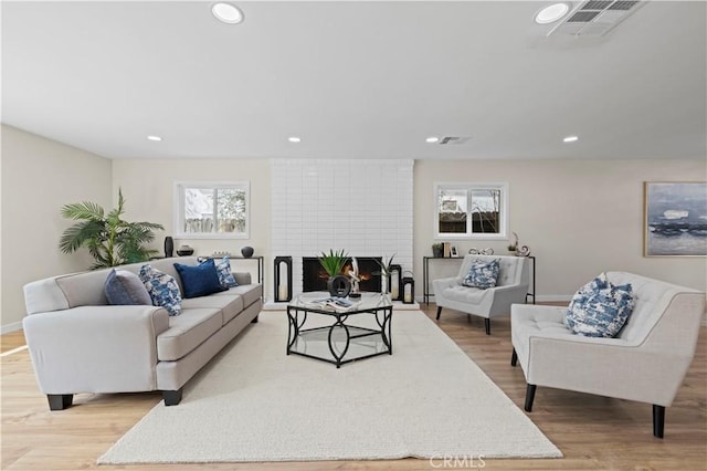 living area with visible vents, recessed lighting, a brick fireplace, and wood finished floors