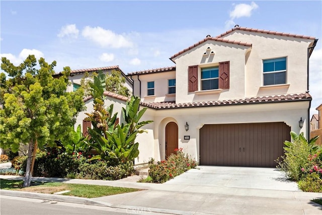 mediterranean / spanish-style home featuring stucco siding, concrete driveway, an attached garage, and a tiled roof