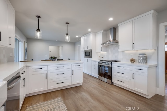 kitchen with light countertops, light wood-style flooring, appliances with stainless steel finishes, a peninsula, and wall chimney exhaust hood