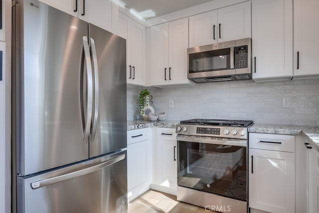 kitchen with white cabinetry, decorative backsplash, light stone counters, and appliances with stainless steel finishes