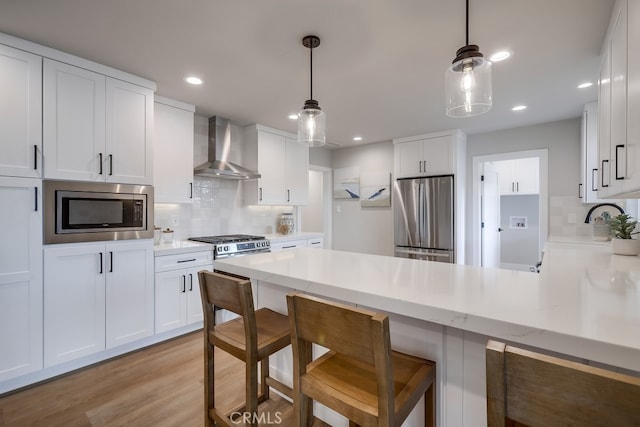 kitchen featuring a peninsula, stainless steel appliances, light wood-style floors, white cabinetry, and wall chimney exhaust hood