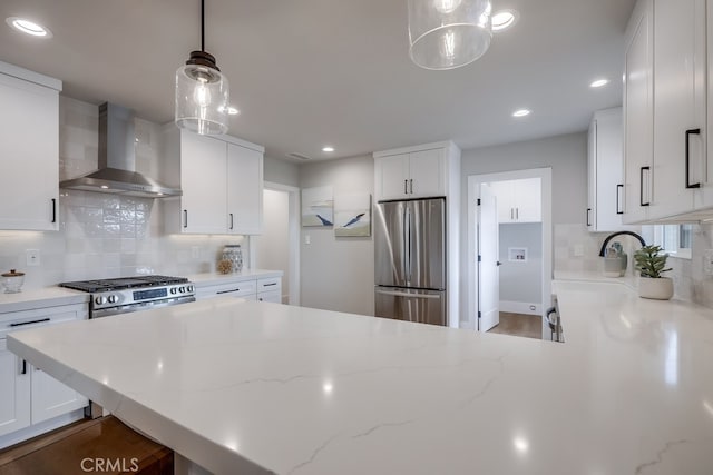 kitchen with a peninsula, stainless steel appliances, decorative backsplash, white cabinets, and wall chimney exhaust hood