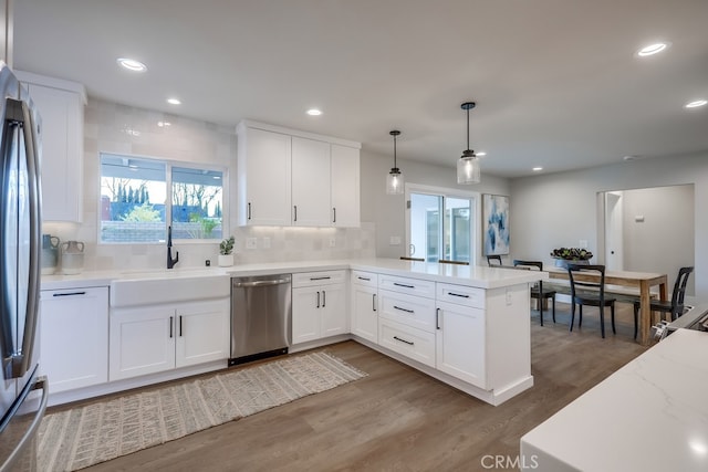 kitchen with wood finished floors, a peninsula, a sink, stainless steel appliances, and white cabinetry