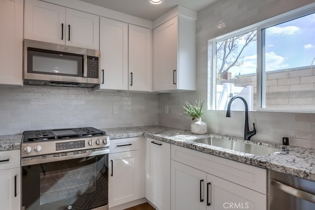 kitchen with a sink, stainless steel appliances, decorative backsplash, and white cabinetry