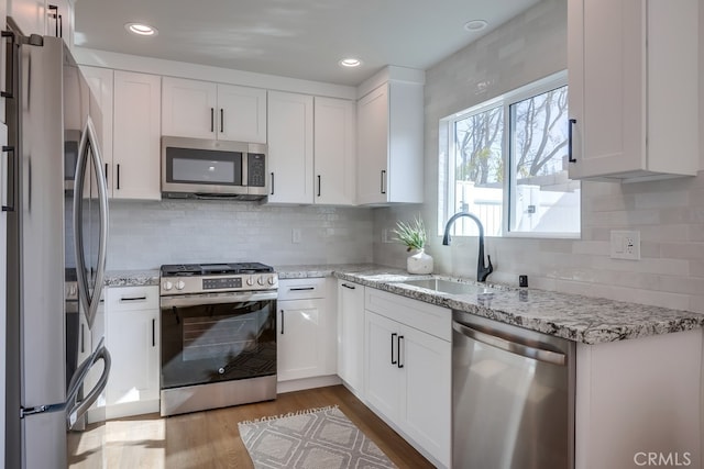 kitchen with a sink, wood finished floors, white cabinetry, and stainless steel appliances