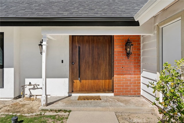 doorway to property with a garage, brick siding, and a shingled roof