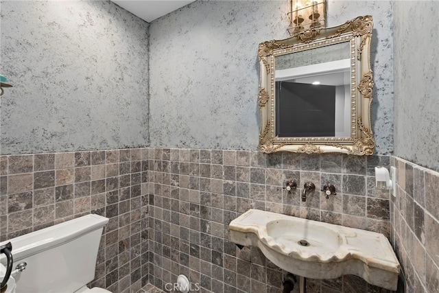 bathroom with a wainscoted wall, wallpapered walls, toilet, and tile walls