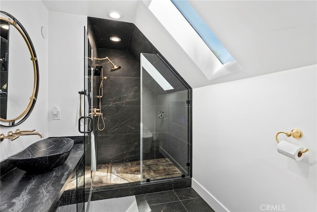 bathroom with baseboards, vaulted ceiling with skylight, a stall shower, a sink, and marble finish floor