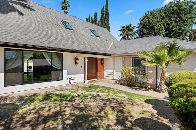 rear view of property featuring a garage, stucco siding, and a shingled roof