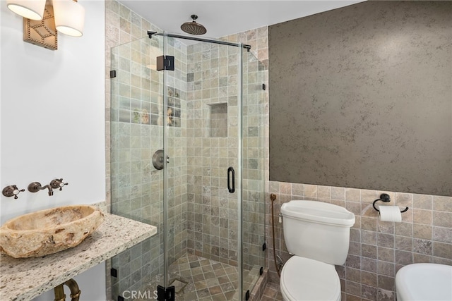 bathroom with a wainscoted wall, a sink, a shower stall, tile walls, and toilet