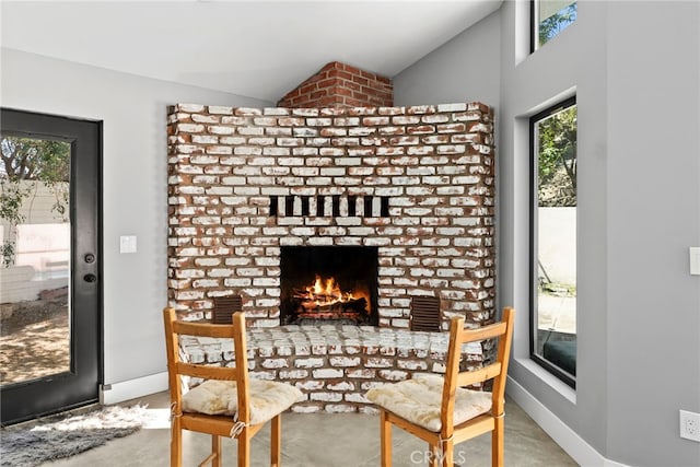 dining room with a brick fireplace, baseboards, concrete flooring, and lofted ceiling