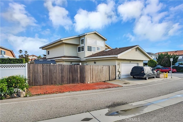 view of side of home featuring a garage, a fenced front yard, and driveway