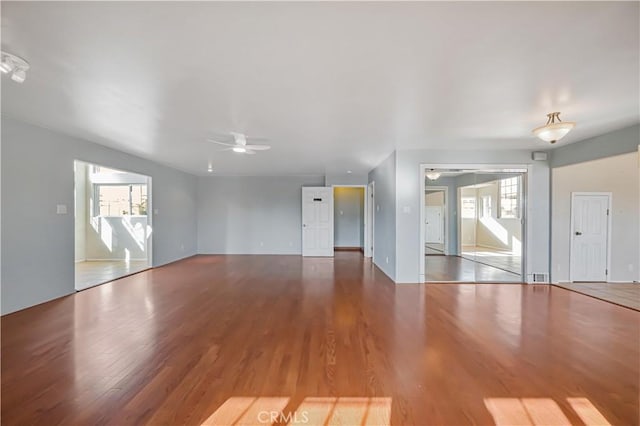 unfurnished living room with plenty of natural light, wood finished floors, and a ceiling fan