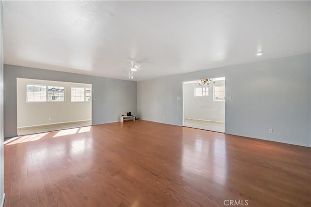 empty room featuring ceiling fan with notable chandelier and wood finished floors