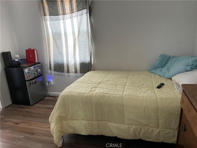 bedroom with wood finished floors, freestanding refrigerator, and baseboards