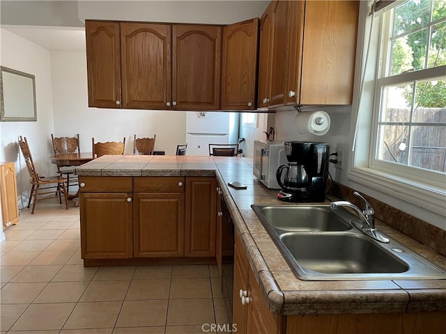 kitchen with a sink, light tile patterned flooring, brown cabinetry, a healthy amount of sunlight, and a peninsula