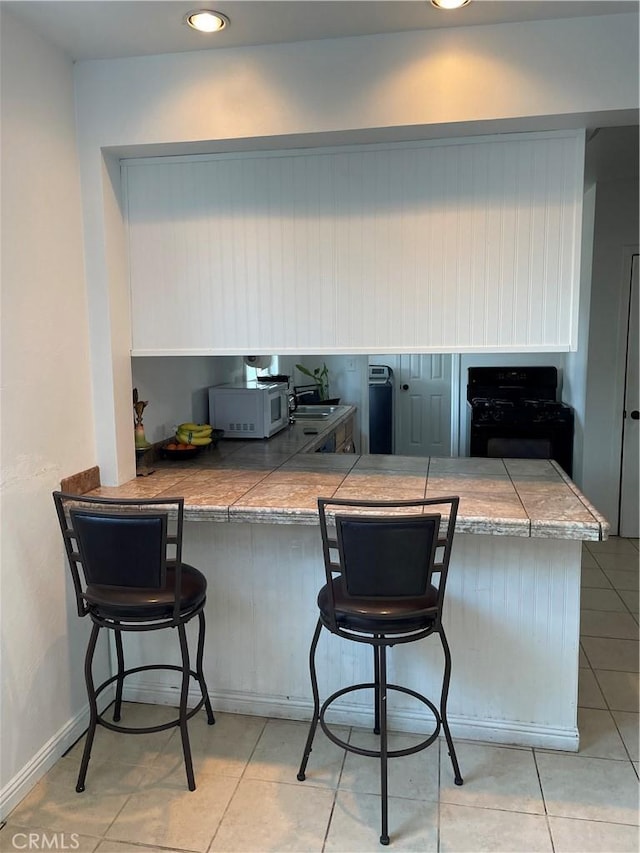 kitchen with a sink, light tile patterned floors, a breakfast bar area, white microwave, and black gas range