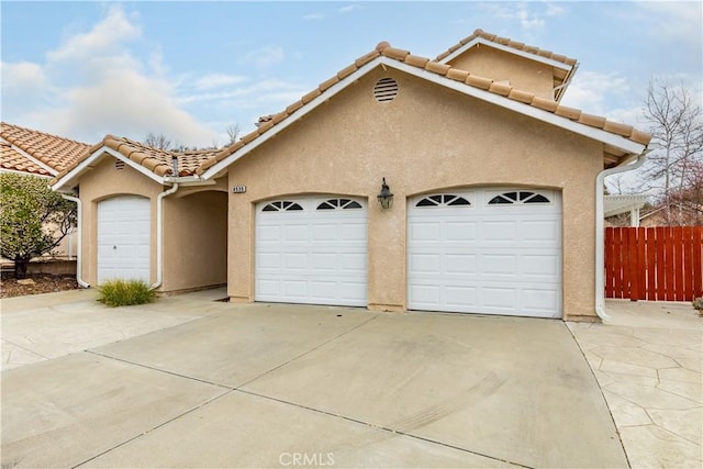 exterior space featuring stucco siding, a tile roof, an attached garage, and fence