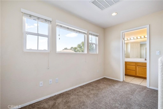 unfurnished bedroom featuring visible vents, light colored carpet, ensuite bathroom, and baseboards