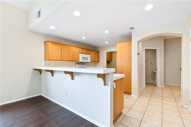 kitchen featuring white microwave, visible vents, a peninsula, tile counters, and a kitchen bar